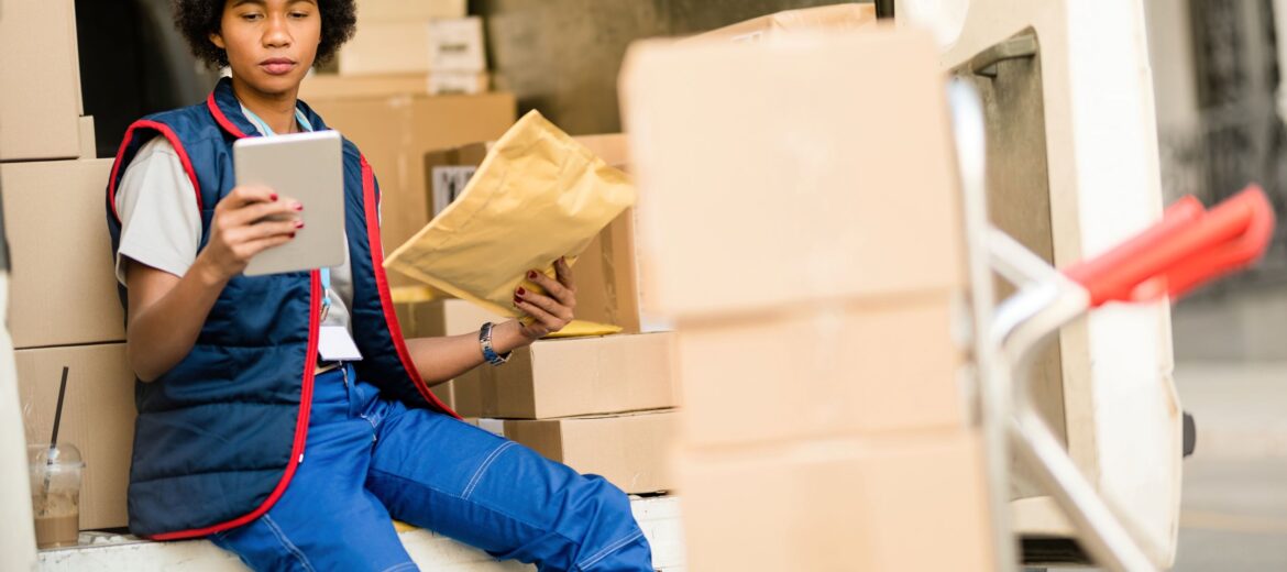 black-female-deliverer-going-through-check-list-touchpad-while-checking-delivery-package-truck